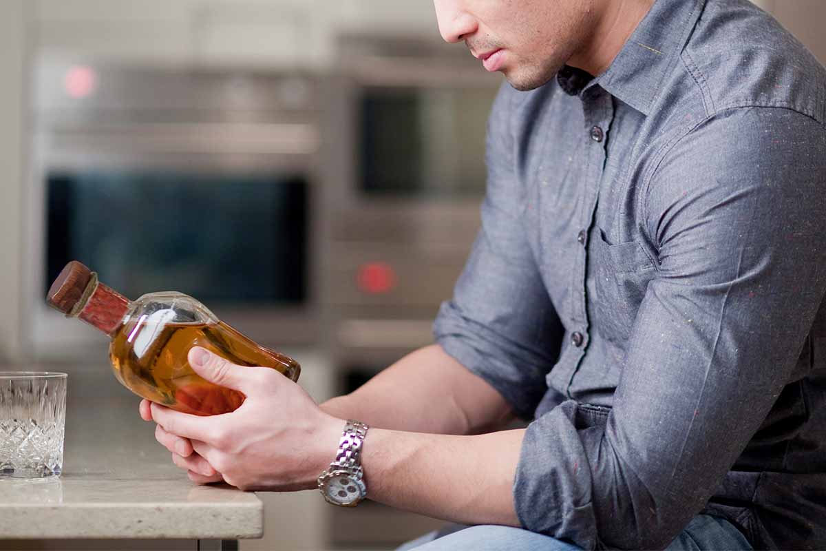 A man examining a whiskey bottle in a kitchen. Nutrition labels may be coming to alcohol bottles.