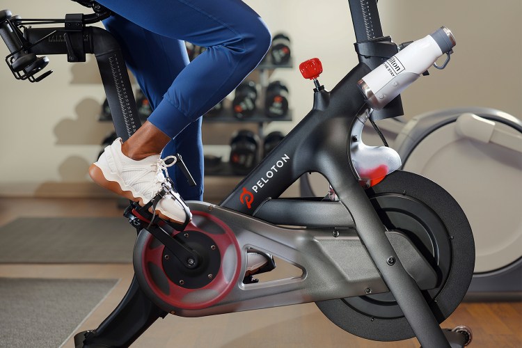A person riding a Peloton Bike in a Hilton hotel with a branded water bottle in the holder