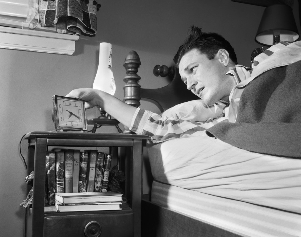 A black and white photo of a 1950s man checking his alarm clock.