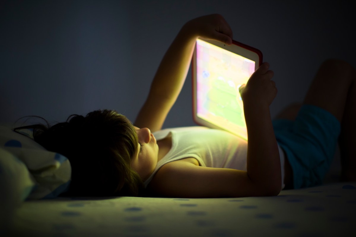 A young child holding an iPad in a dark bedroom.