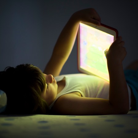 A young child holding an iPad in a dark bedroom.