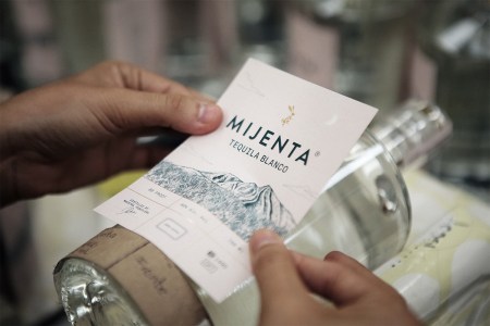 A hand placing the label on a bottle of Mijenta Tequila