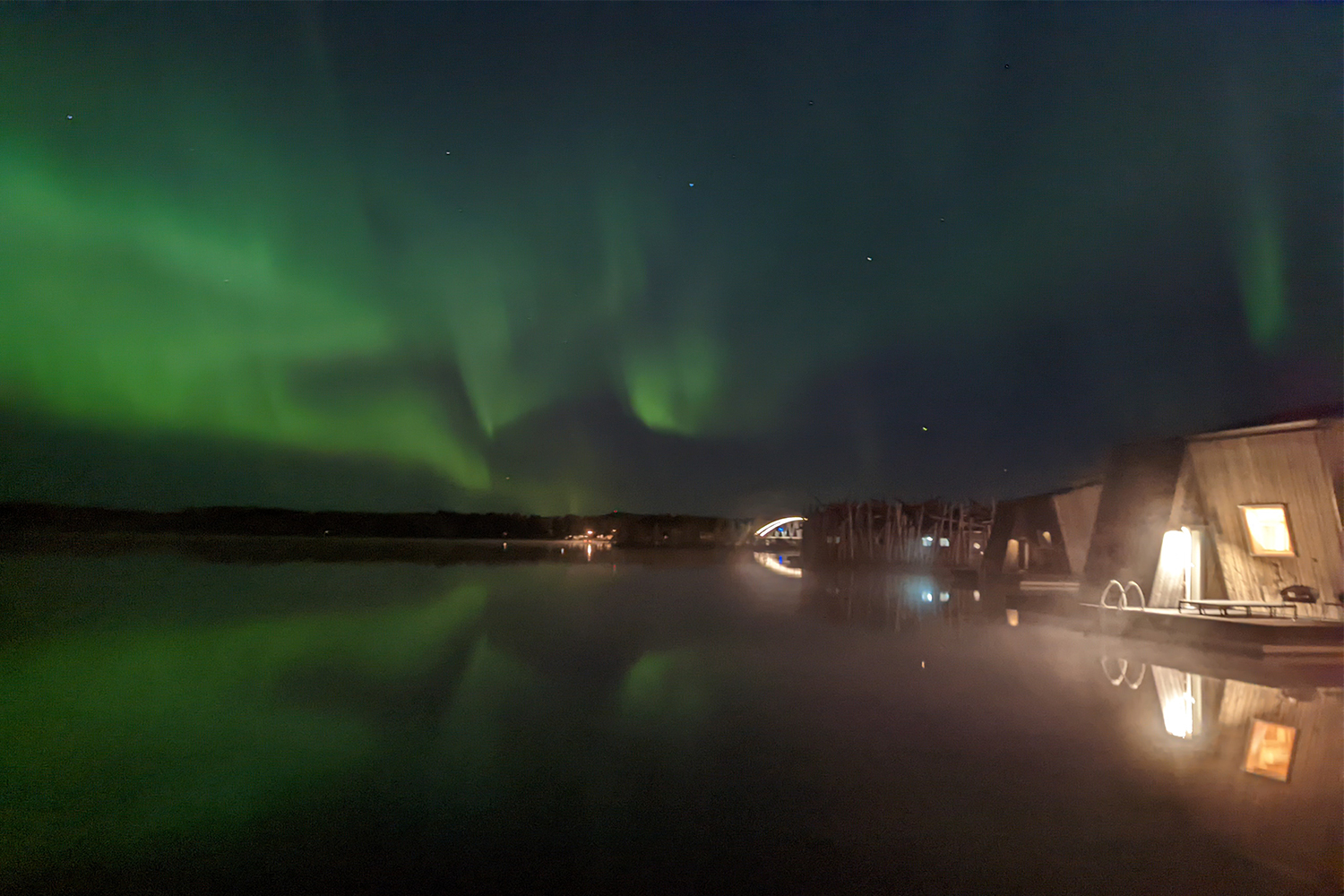 The green northern lights in the night sky over the water at Arctic Bath, a boutique hotel in Sweden