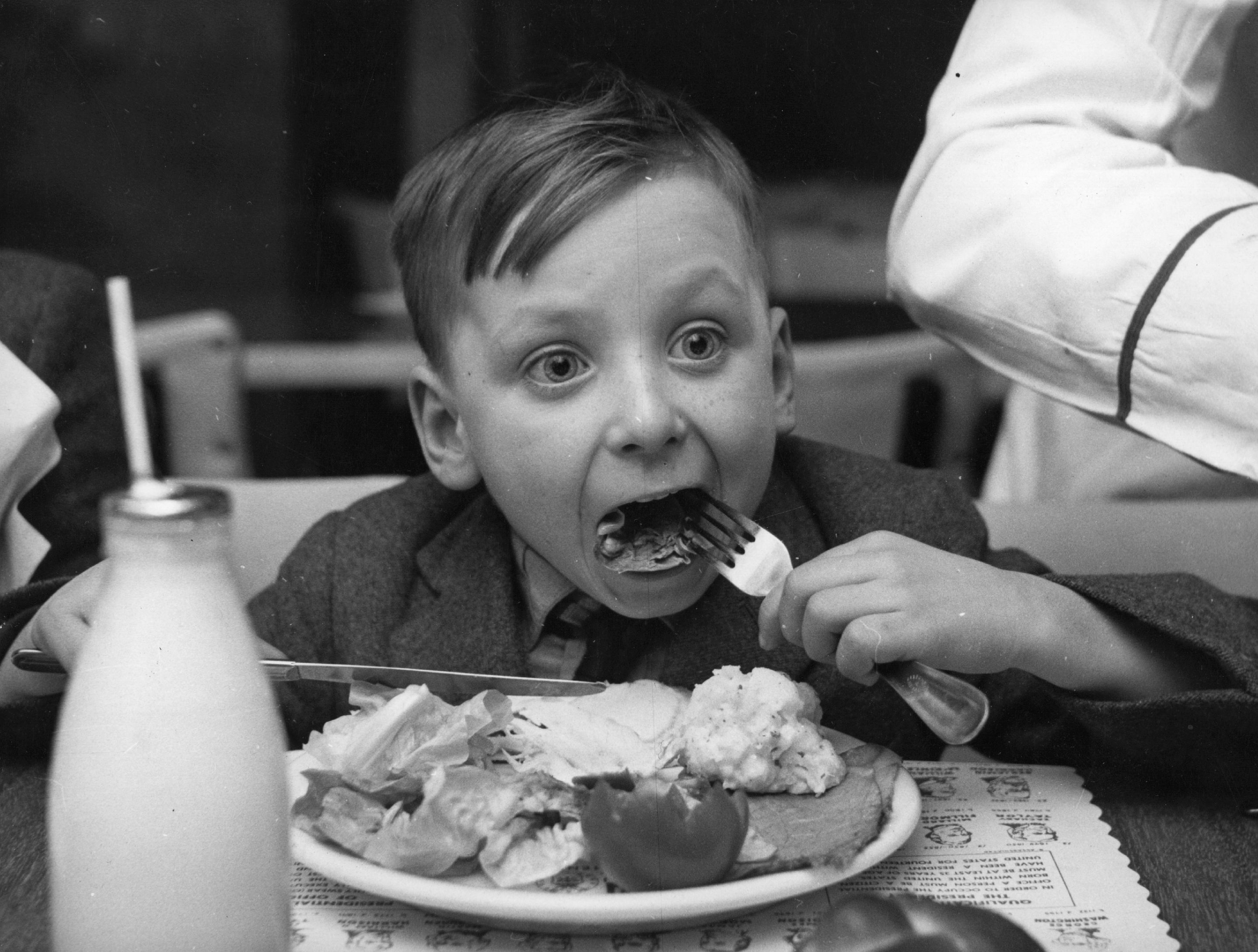A little boy eating a plate full of food with his eyes wide.