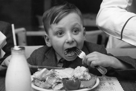 A little boy eating a plate full of food with his eyes wide.
