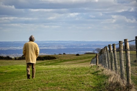 A man walking next to a fence on a farm.