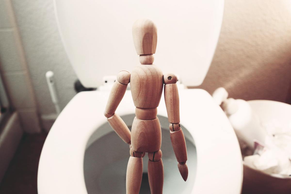 Wooden sculpture standing on a toilet seat and"peeing."