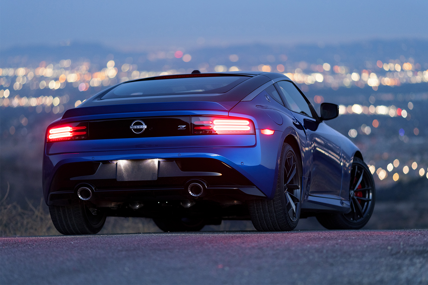 The rear end of the new 2023 Nissan Z sports car, in blue, shown here with the red taillights illuminated at dusk