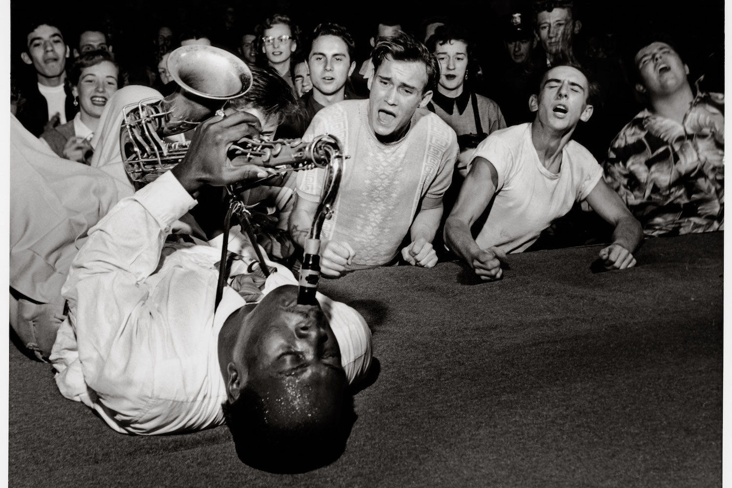 Big Jay McNeely lying on the stage playing his saxophone in front of screaming fans