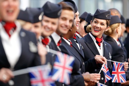 British Airways flight attendants standing in a line wearing their uniforms and holding Union Jack flags
