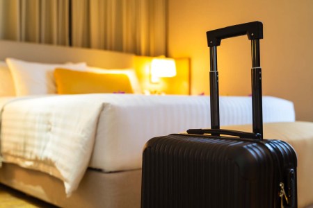 A black suitcase sitting in front of a bed in a hotel room. A new survey looks at the number of mattresses stolen from hotels.