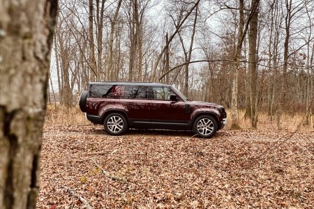 A maroon Land Rover in the woods in fall with lots of leaves