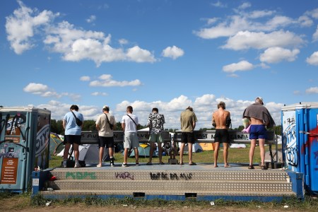 A row of men peeing outside at a music festival.