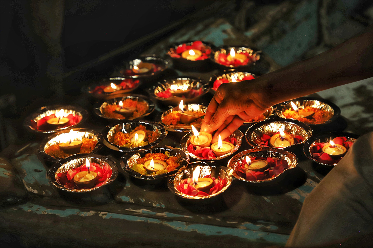 A hand reaches down to grab a bowl holding a candle in Varanasi, India, at night