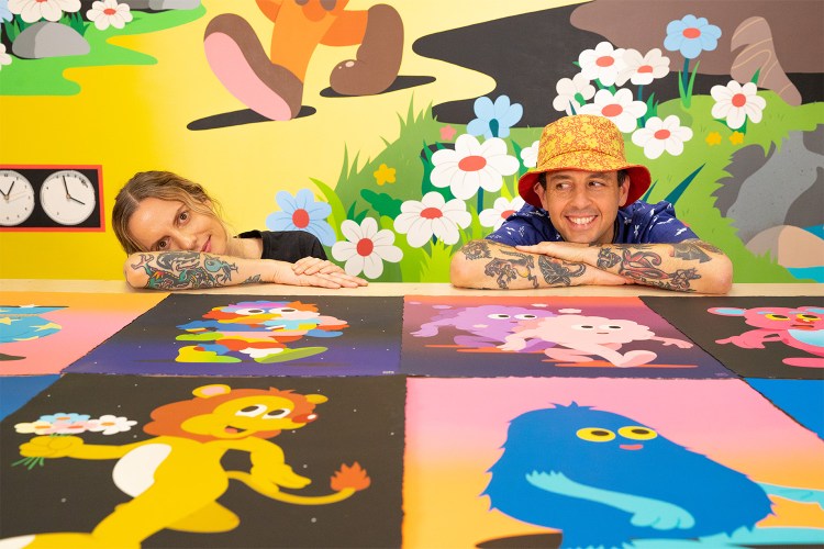 The husand-and-wife duo DABSMYLA, Darren and Emmelene Mate, sit with their artwork for the show "In Technicolor"