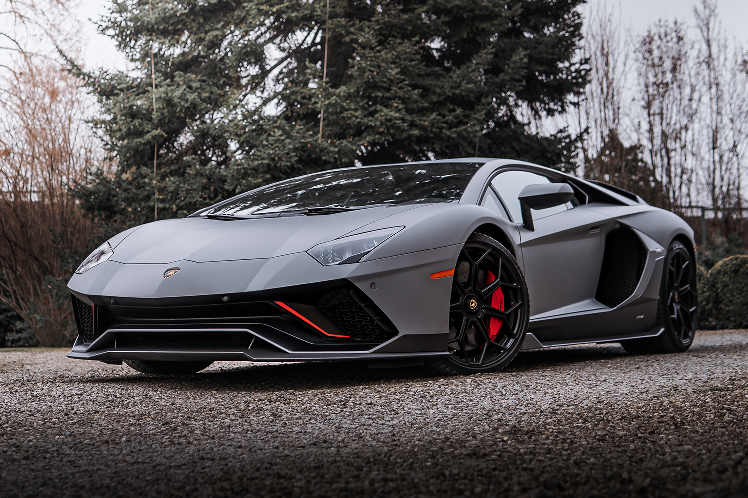 The Aventador LP 780-4 Ultimae in grey with red and black accents sits still on a gravel drivea