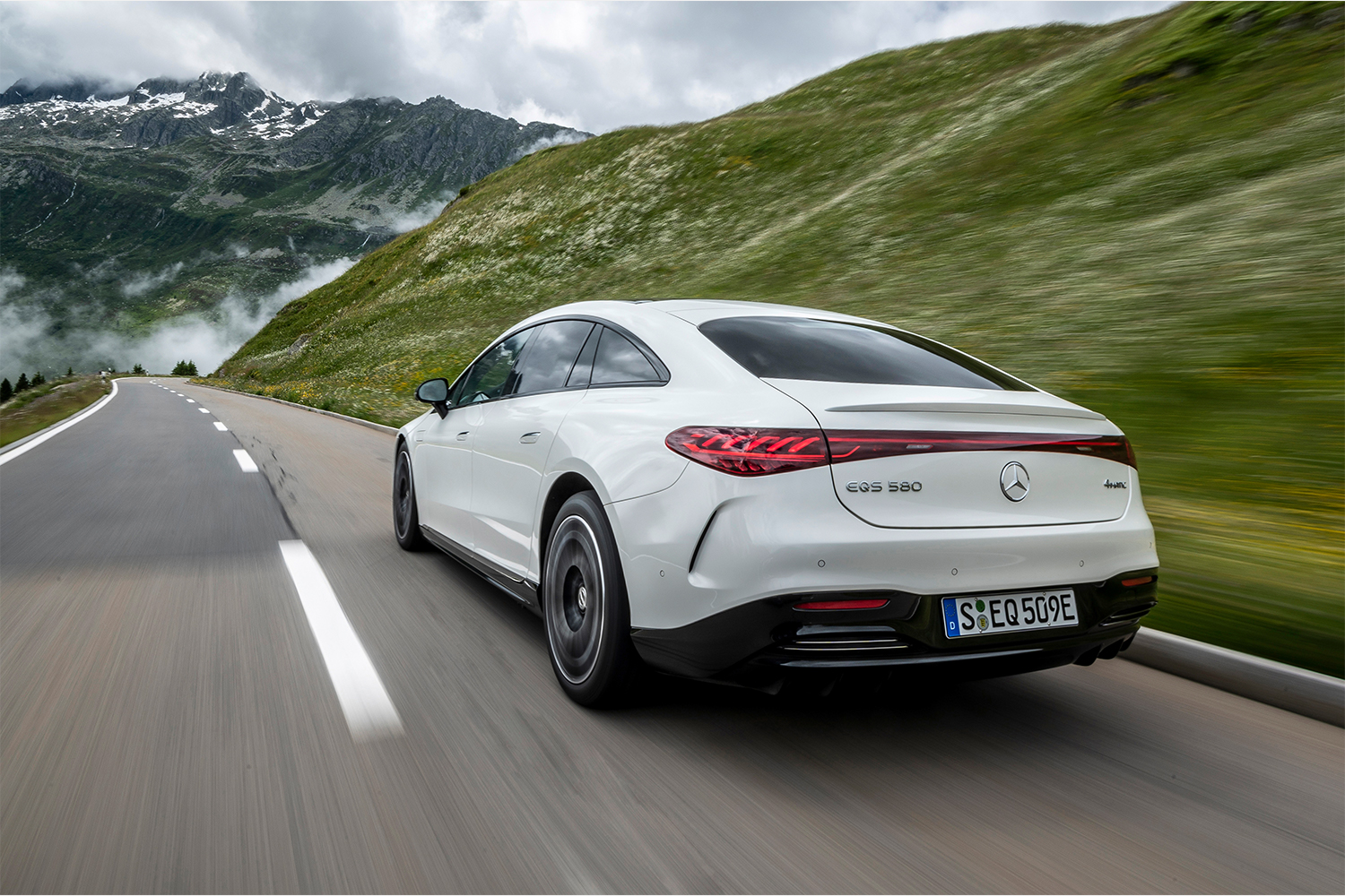 A white Mercedes-Benz EQS 580 4MATIC in white is shown driving down a mountain road. We reviewed the luxury electric sedan.