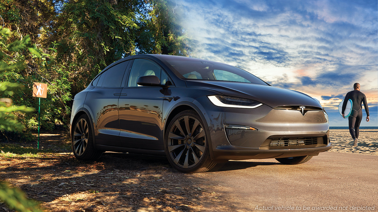 A Tesla Model X Plaid sitting on a path next to a sandy beach with a surfer in the background