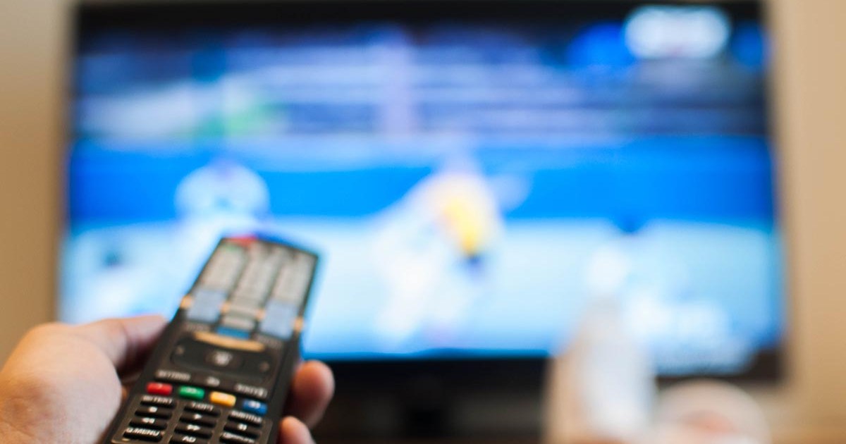 A person holding a TV remote and looking at a blurry screen while holding a TV remote. There are several settings you should change on your TV as soon as you get a new one.