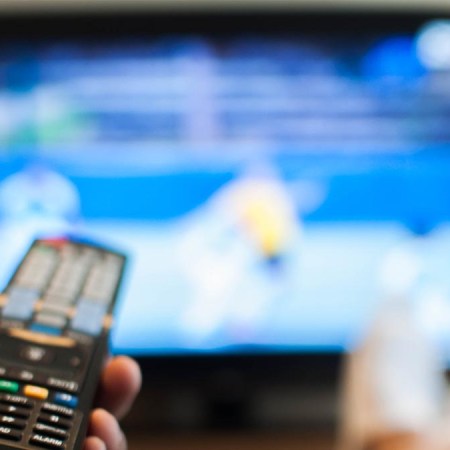 A person holding a TV remote and looking at a blurry screen while holding a TV remote. There are several settings you should change on your TV as soon as you get a new one.
