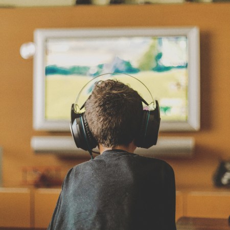 A boy with a headset playing video games on the TV, his back to the camera.