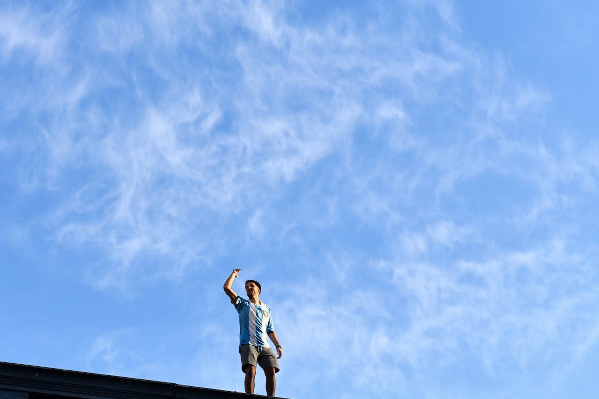 An Argentinian soccer fan standing on a roof in celebration.