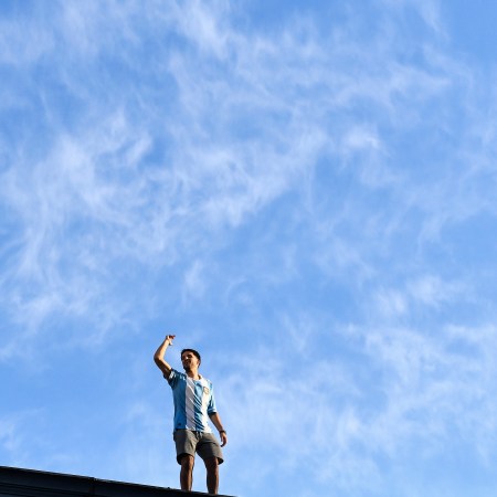An Argentinian soccer fan standing on a roof in celebration.