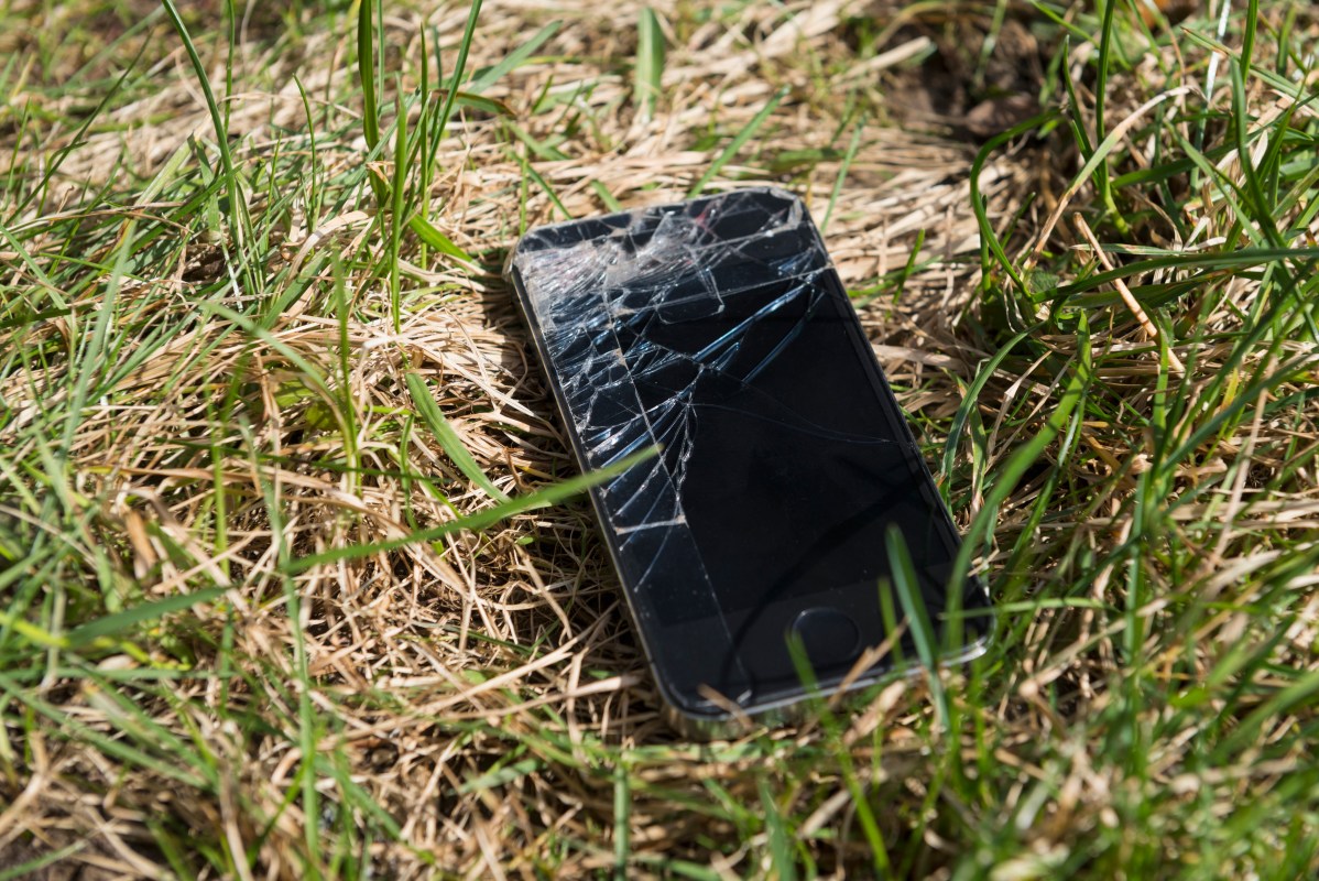 A shattered smartphone lying in a patch of grass.