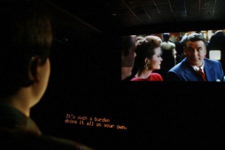 A picture of a man watching TV with closed captioning on.