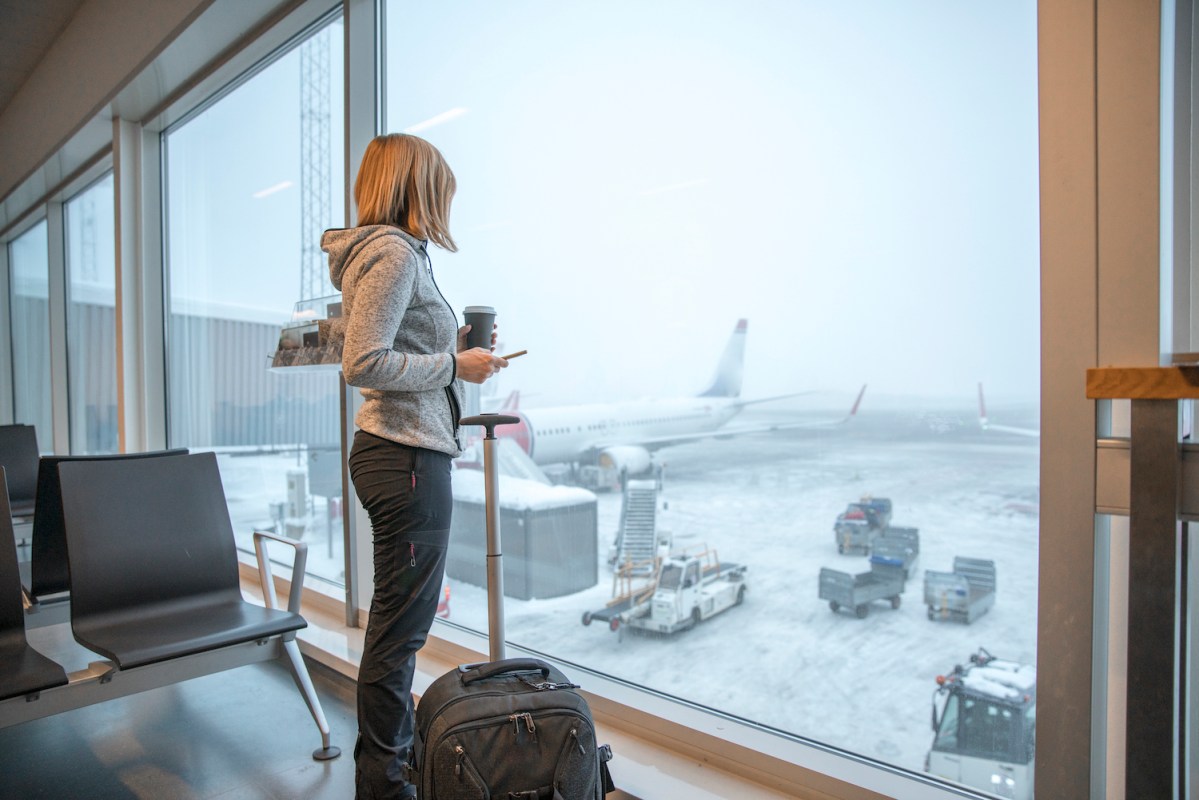 Woman standing close to a window at an airport covered in snow