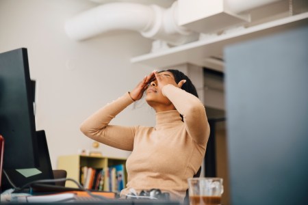 Frustrated female worker rubbing her eyes in front of a computer sitting in creative office