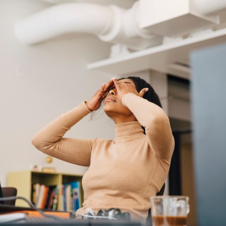 Frustrated female worker rubbing her eyes in front of a computer sitting in creative office