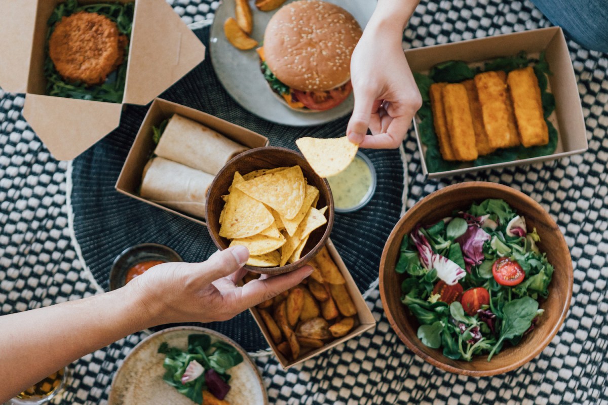 overhead shot of a takeout meal including a burger, salad and tortilla chips