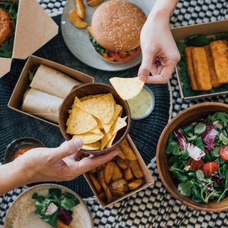 overhead shot of a takeout meal including a burger, salad and tortilla chips