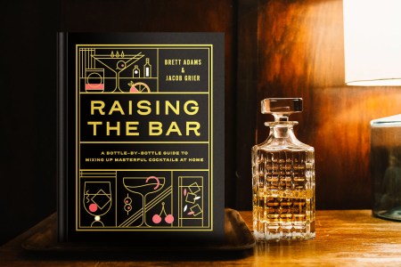 The cocktail book Raising the Bar on a table in a dimly lit room with a decanter