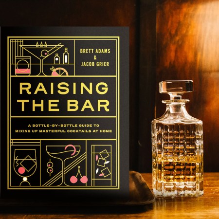 The cocktail book Raising the Bar on a table in a dimly lit room with a decanter