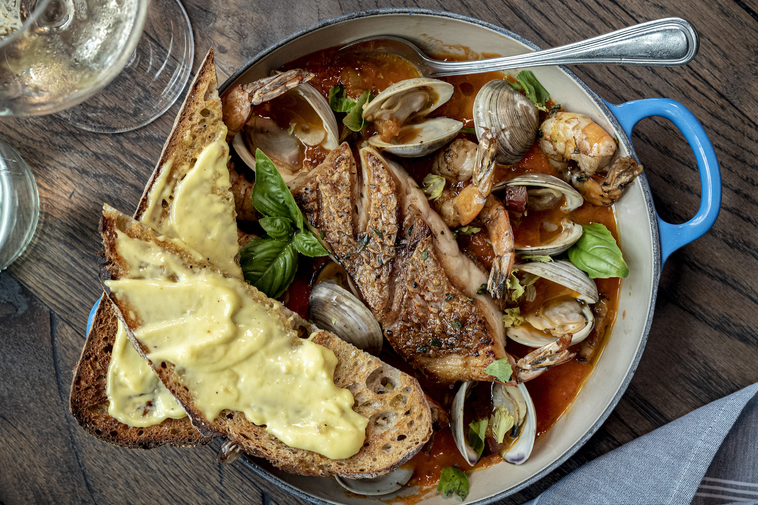 cioppino in a blue dutch oven with toasted bread and a glass of white wine