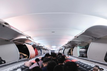 Passengers boarding an airplane with the baggage compartments open. A flight attendant explains why you should be the last person to board a plane.