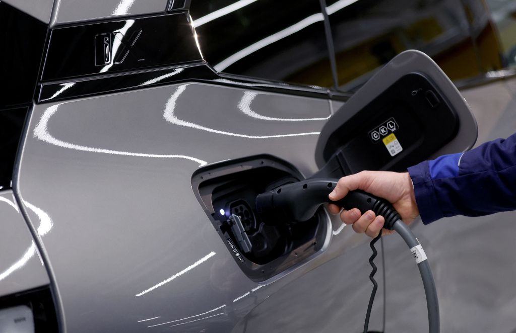A hand holding an EV charger into the charging port of an electric car
