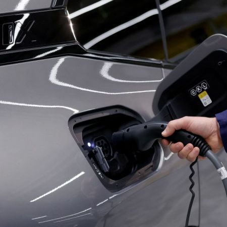 A hand holding an EV charger into the charging port of an electric car