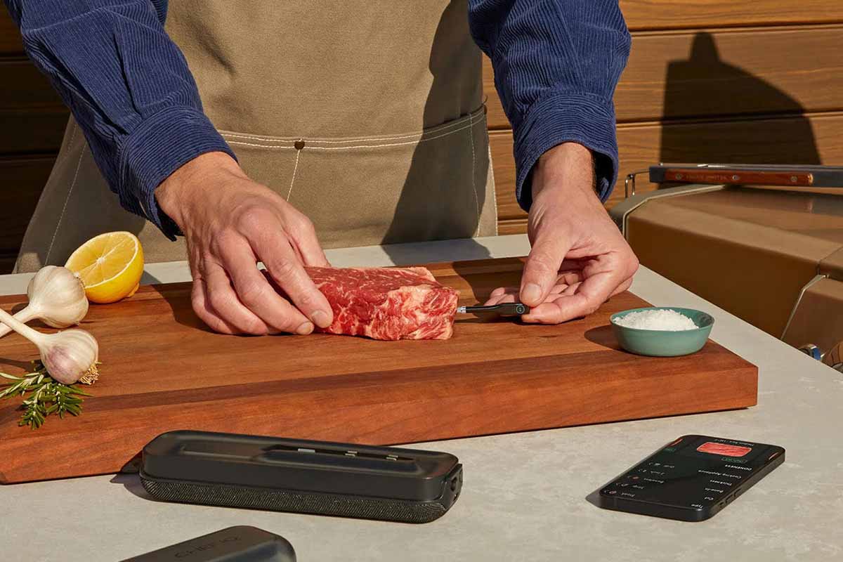 CHEF iQ Smart Thermometer, on a table being used by someone inserting the probe into a steak