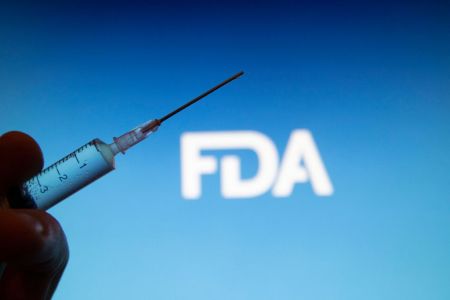 A syringe and needle in front of the FDA logo on a blue screen