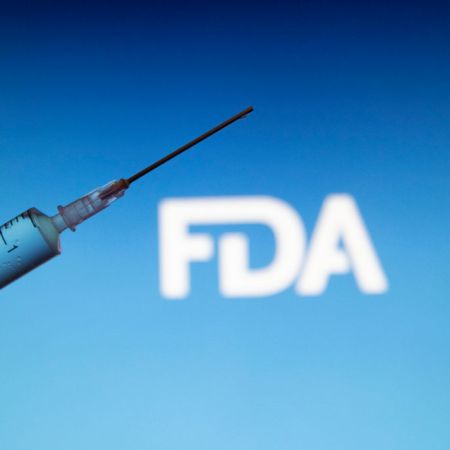 A syringe and needle in front of the FDA logo on a blue screen