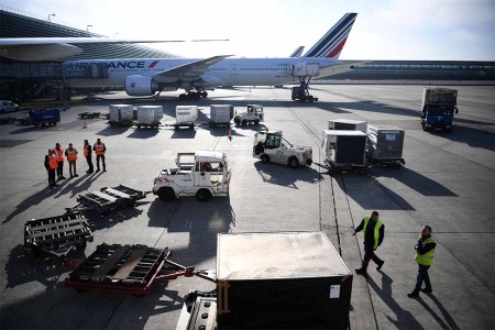 This picture taken on November 10, 2022 shows custom officials (L) monitoring as airfreight is downloaded from a Boeing 777 aircraft docked at its station at Roissy-Charles de Gaulle airport outside Paris. A new law will limit domestic flights due to CO2 emissions