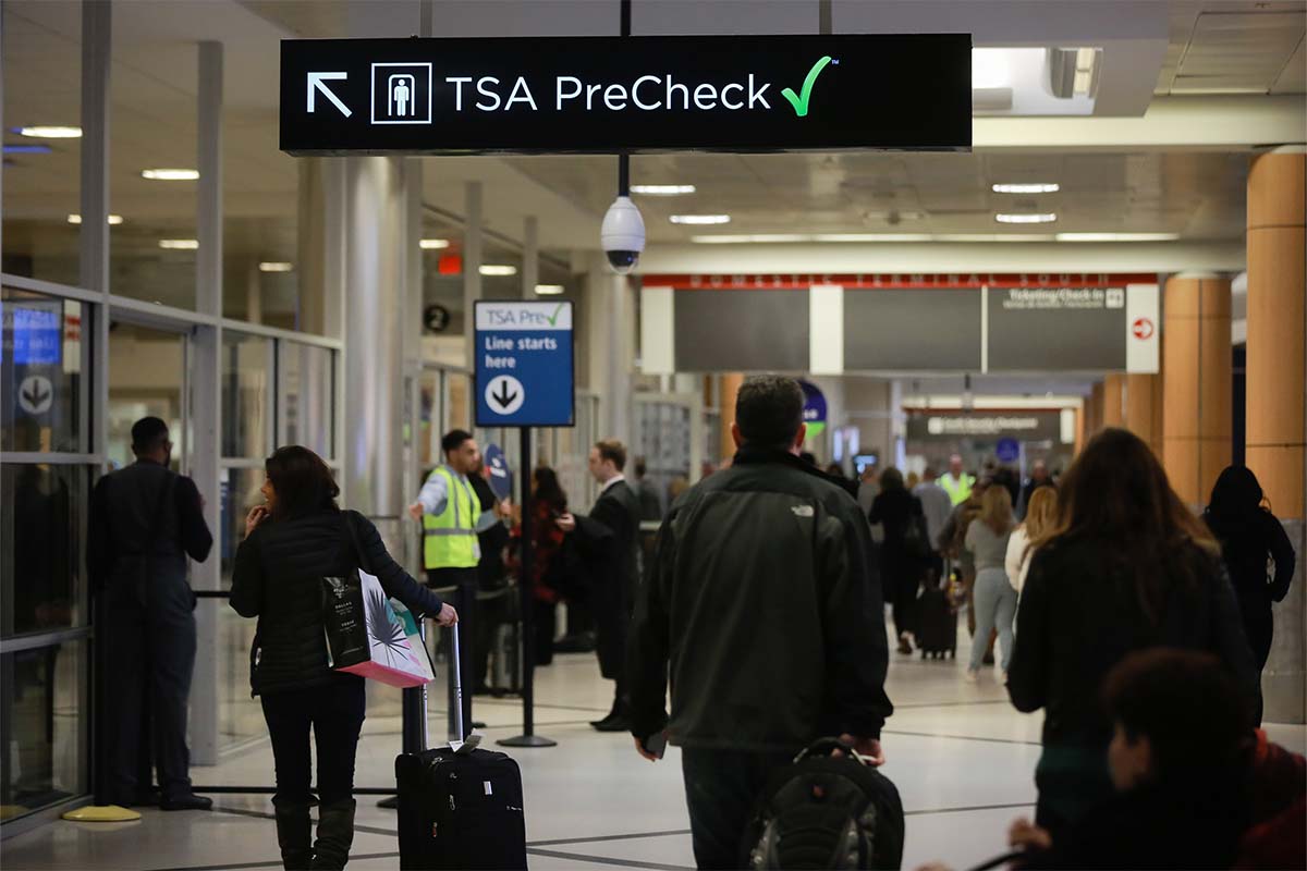 Travelers pass under a sign pointing toward a Transportation Security Administration (TSA) Pre-Check checkpoint at an airport. The application process for TSA PreCheck is backlogged, but there might be a way to get an interview more quickly.