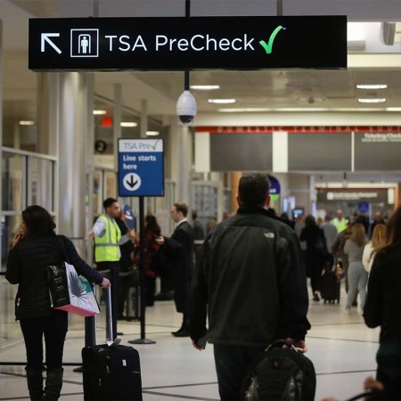 Travelers pass under a sign pointing toward a Transportation Security Administration (TSA) Pre-Check checkpoint at an airport. The application process for TSA PreCheck is backlogged, but there might be a way to get an interview more quickly.