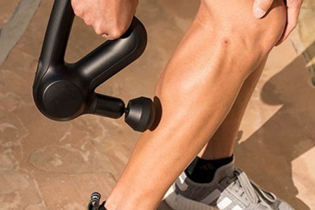 A person using a Theragun massage device on their bare leg