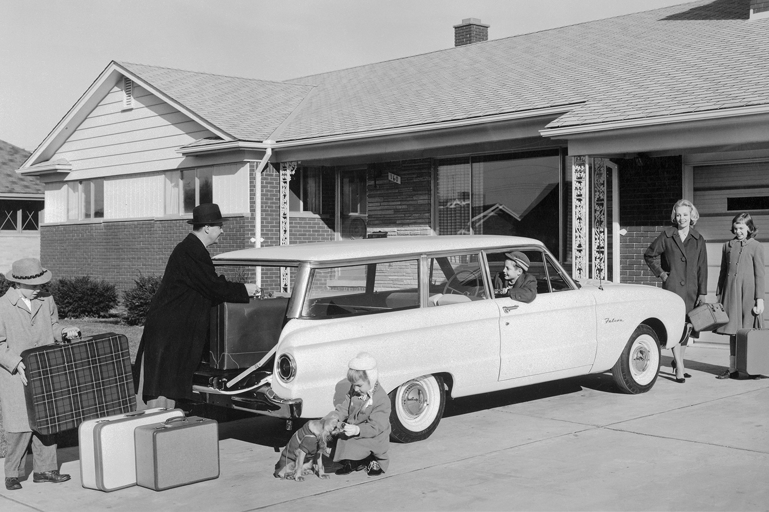 A black and white photo of a family packing bags in a 1960 Ford Falcon station wagon ahead of a trip