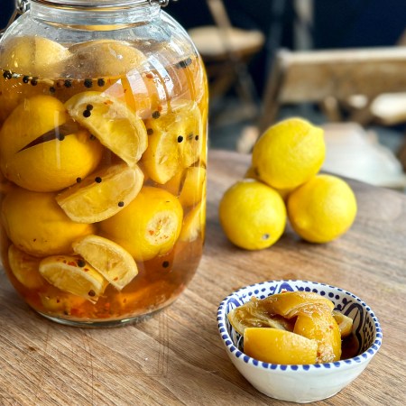 a jar and bowl of preserved lemons sitting on a wooden table
