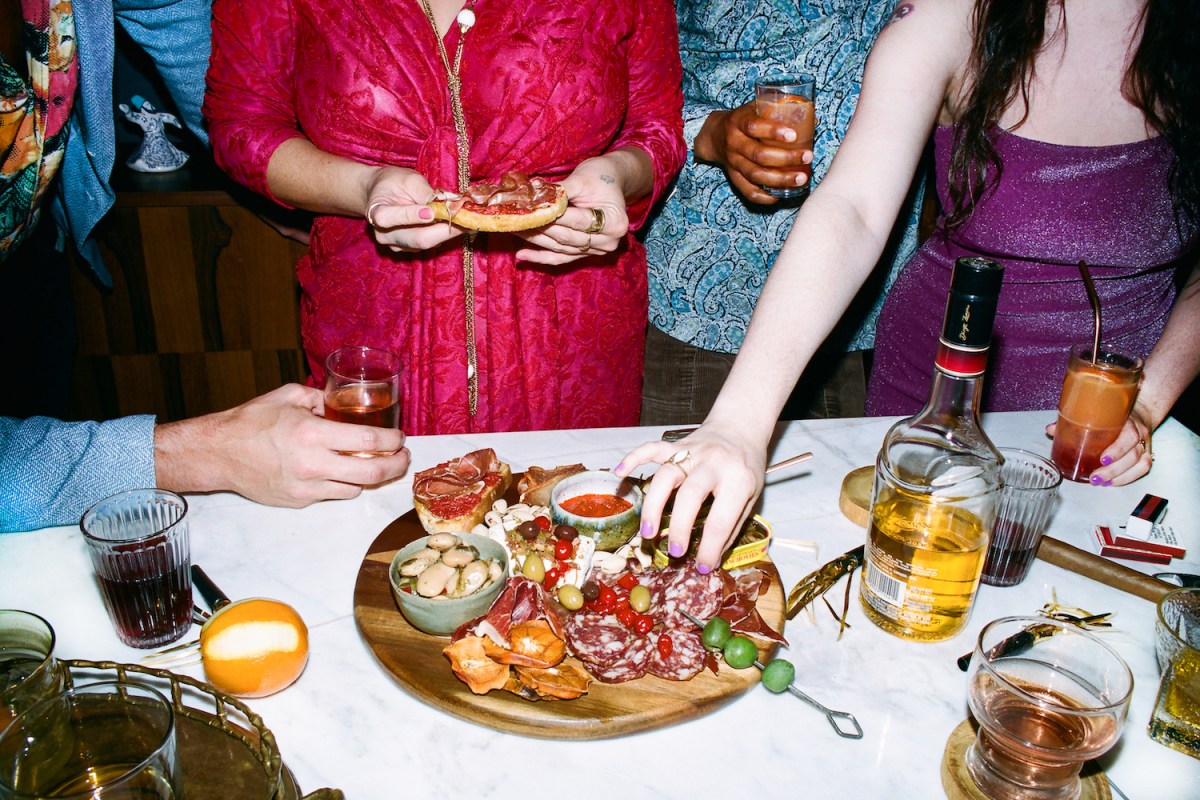 people standing around a table with cocktails eating from a charcuterie platter